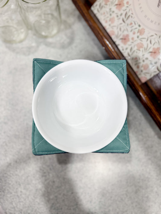 White bowl on a teal placemat with a floral tablecloth in the background