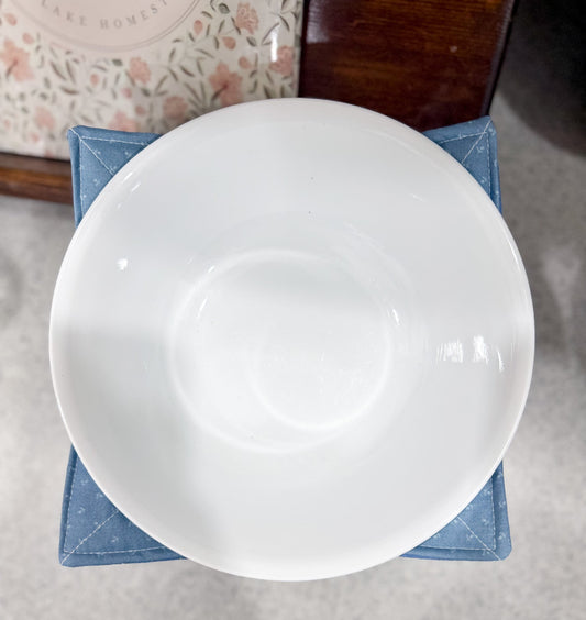 White ceramic bowl on a textured surface with a floral-patterned object in the background