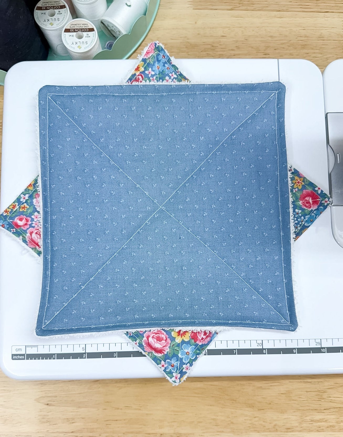 Blue quilted square with floral corners on a sewing machine