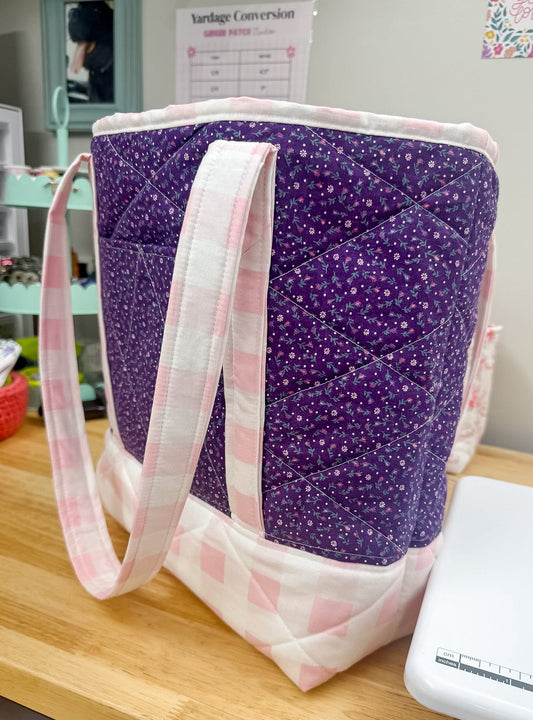 Purple quilted bag with pink handles on a wooden surface