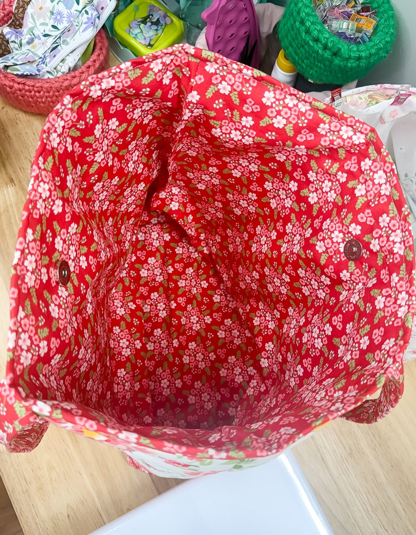 Red floral-patterned fabric on a wooden surface with various items in the background.