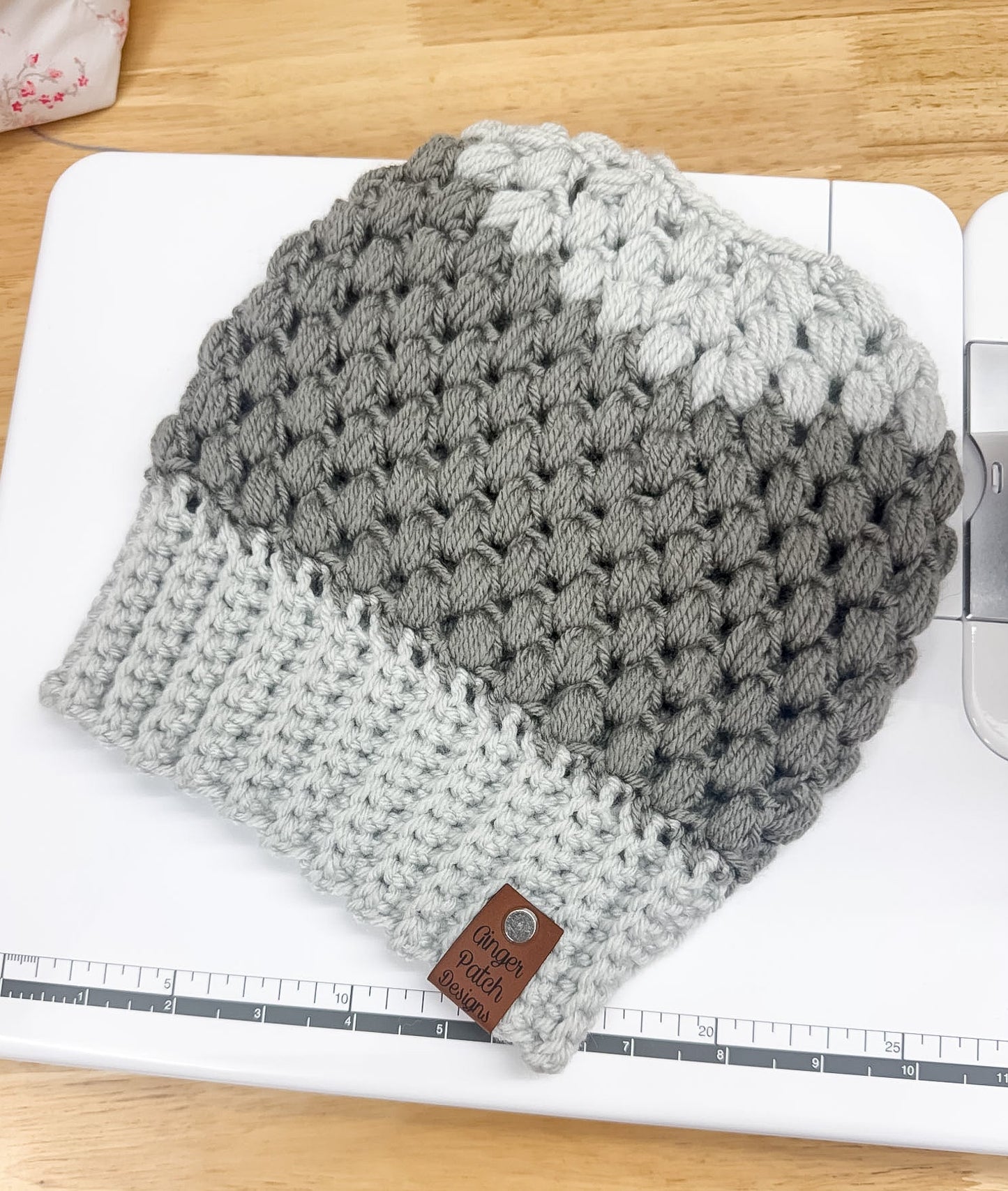 Gray and white knitted beanie on a white surface with a ruler for scale.