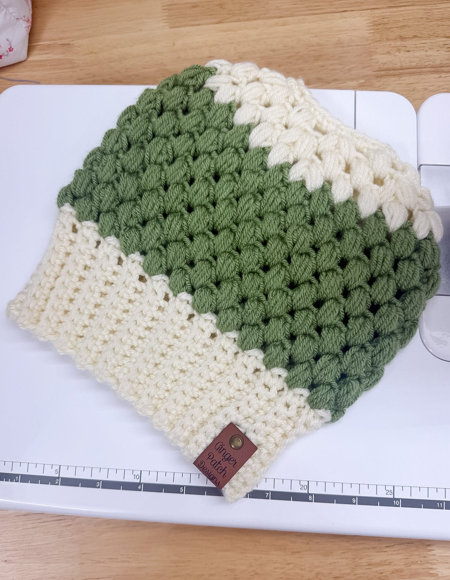 Green and white crocheted beanie with a brown leather tag on a white surface.