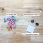 A flat lay of sewing and quilting accessories on a light wood background, including a pile of colorful sewing clips, a 18mm magnetic snap set, and white cotton batting squares with text labels.