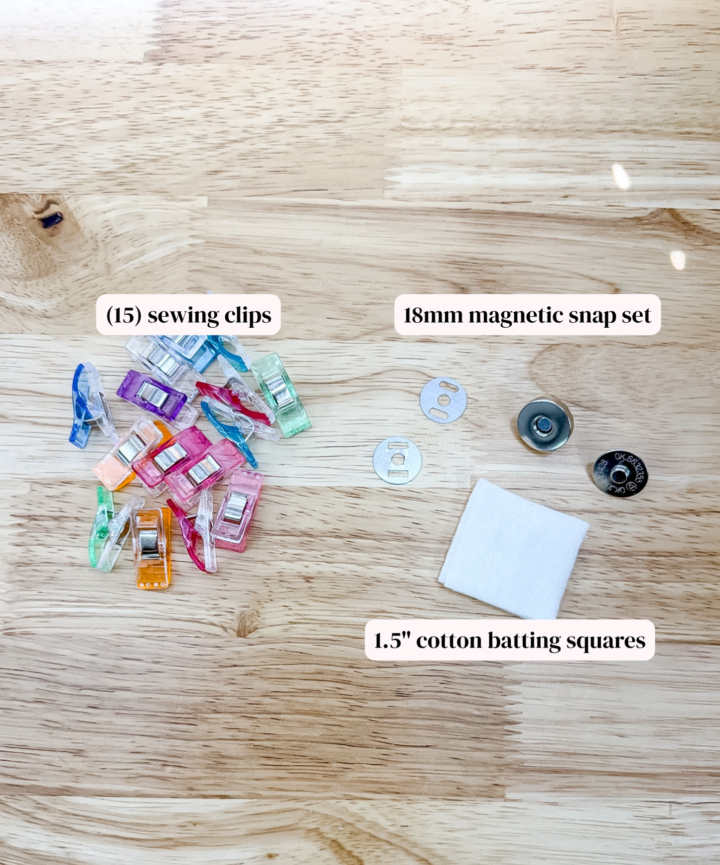 A flat lay of sewing and quilting accessories on a light wood background, including a pile of colorful sewing clips, a 18mm magnetic snap set, and white cotton batting squares with text labels.