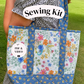 A person outdoors carrying a large quilted tote bag with a floral print. The bag has blue borders and handles, and the front panels show a multicolor floral pattern on a light background.