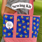 A person outdoors carrying a large fabric tote bag with red-and-white gingham trim and blue front panels printed with small red and yellow floral motifs. A white label on the bag reads 'PDF & VIDEO', and a white banner across the top says 'Sewing Kit'.