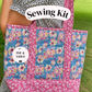 A person outdoors carrying a floral sewing tote bag. The bag has pink floral trim and panels with blue center panels featuring pink, yellow, and white flowers.