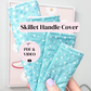 A hand holds three quilted fabric handle covers in a light aqua blue color with a small white floral pattern. The image features text overlays reading 'Skillet Handle Cover' and 'PDF & VIDEO'.