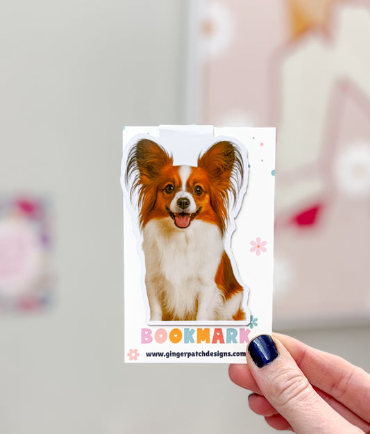 Dog bookmark with colorful text held by a hand against a blurred background