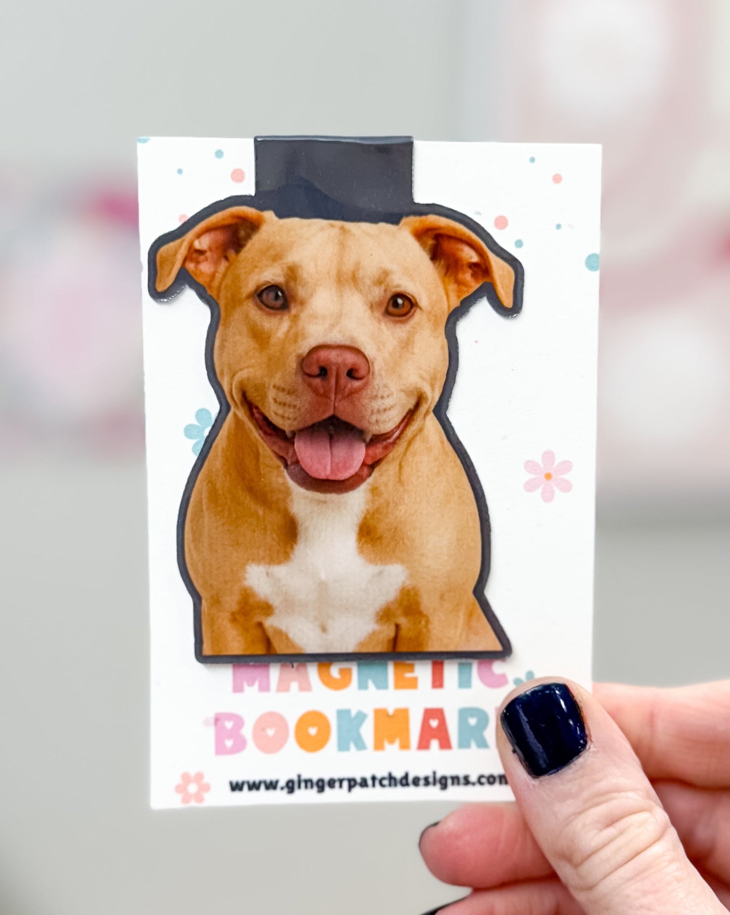Dog-shaped magnetic bookmark held by a hand with a blurred background