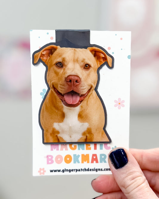 Dog-shaped magnetic bookmark held by a hand with a blurred background
