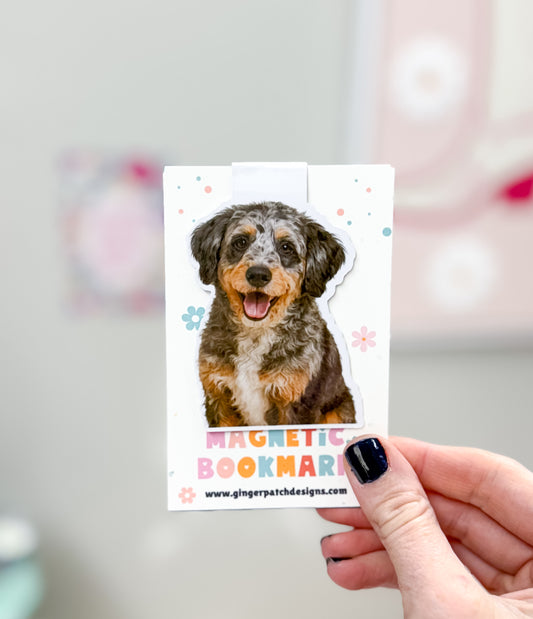 Dog-themed magnetic bookmark held by a hand with a blurred background