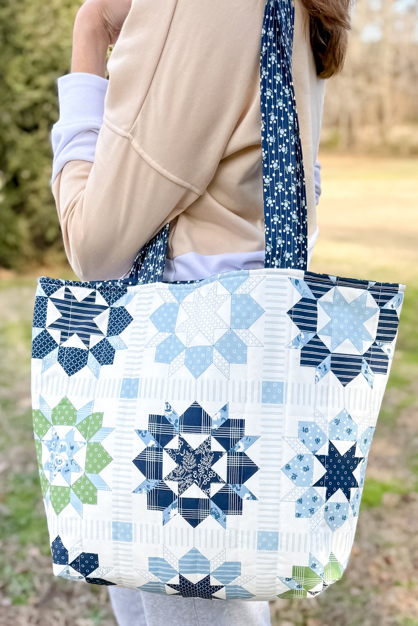 Person holding a quilted tote bag with star patterns in blue and green.