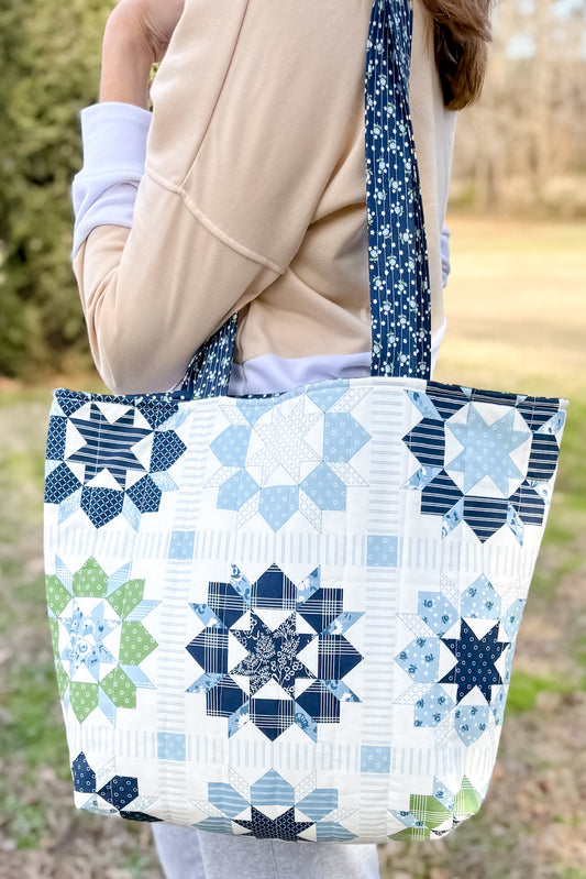 Person holding a quilted tote bag with star patterns in blue and green.