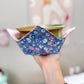 Hand holding a small floral-patterned bowl with a blurred background
