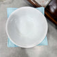 White ceramic bowl on a light blue napkin with a floral-patterned surface in the background