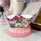 Pink pet bowl with floral patterned cover on a textured surface