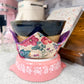 Decorative pink stand with a floral fabric cover holding a black bowl.