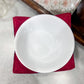 White bowl on a red napkin with a floral-patterned tablecloth in the background