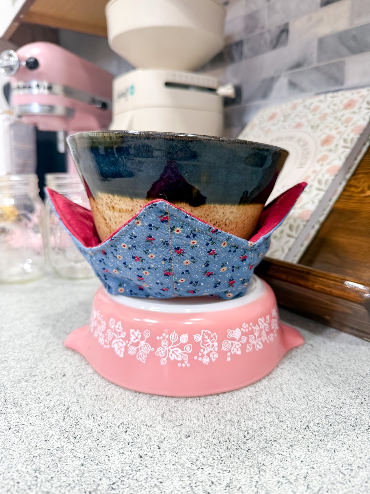 Ceramic pot with a blue floral cover on a pink stand in a kitchen setting