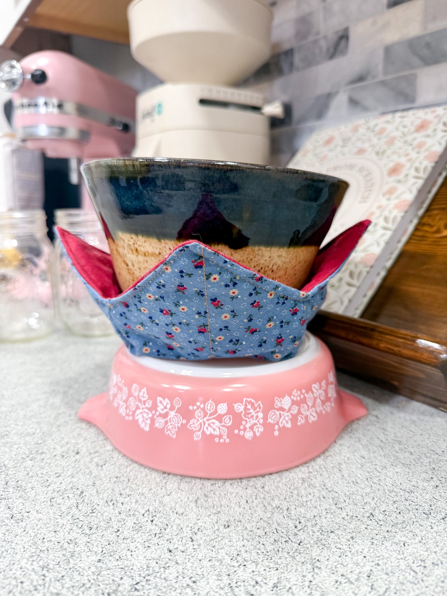 Ceramic pot with a blue floral cover on a pink stand in a kitchen setting