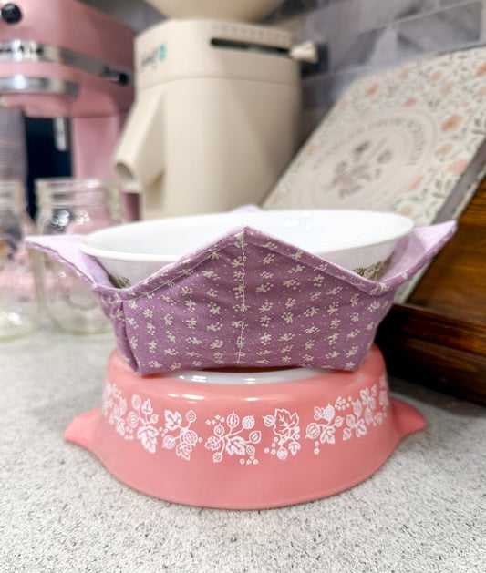 Pink and white decorative bowl with a purple lid on a kitchen counter.