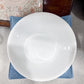 White ceramic bowl on a textured surface with a floral-patterned object in the background