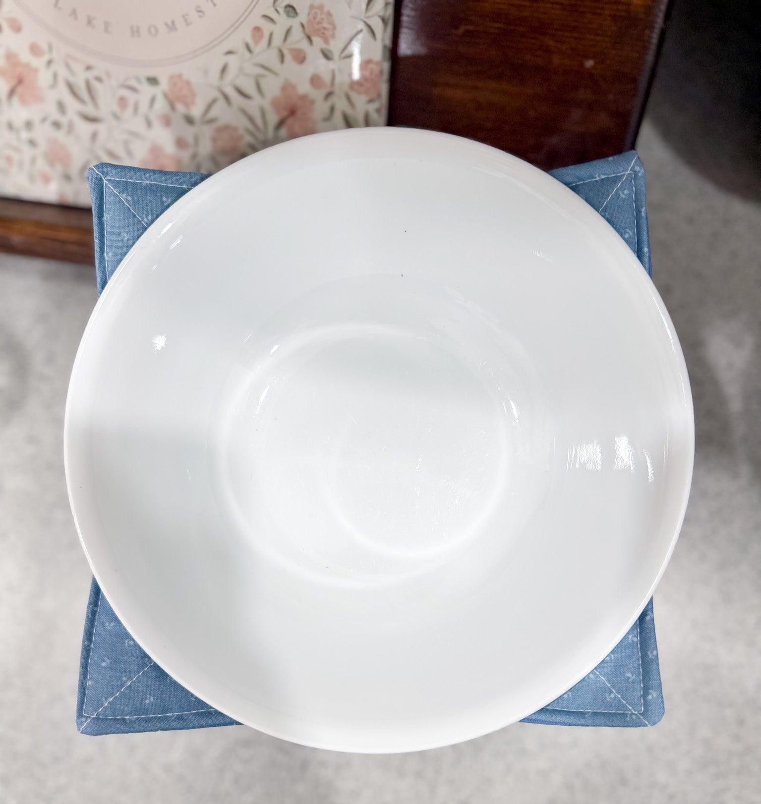 White ceramic bowl on a textured surface with a floral-patterned object in the background