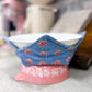 Decorative bowl with floral design on a pink stand on a countertop.