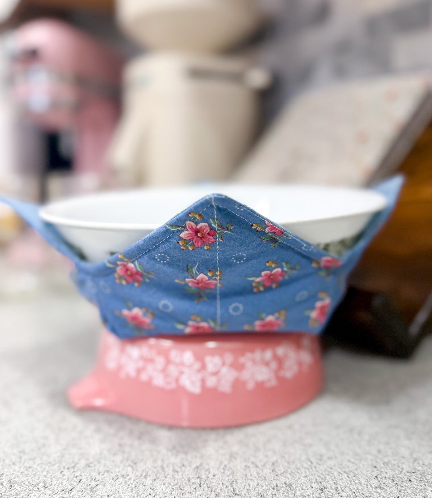 Decorative bowl with floral design on a pink stand on a countertop.