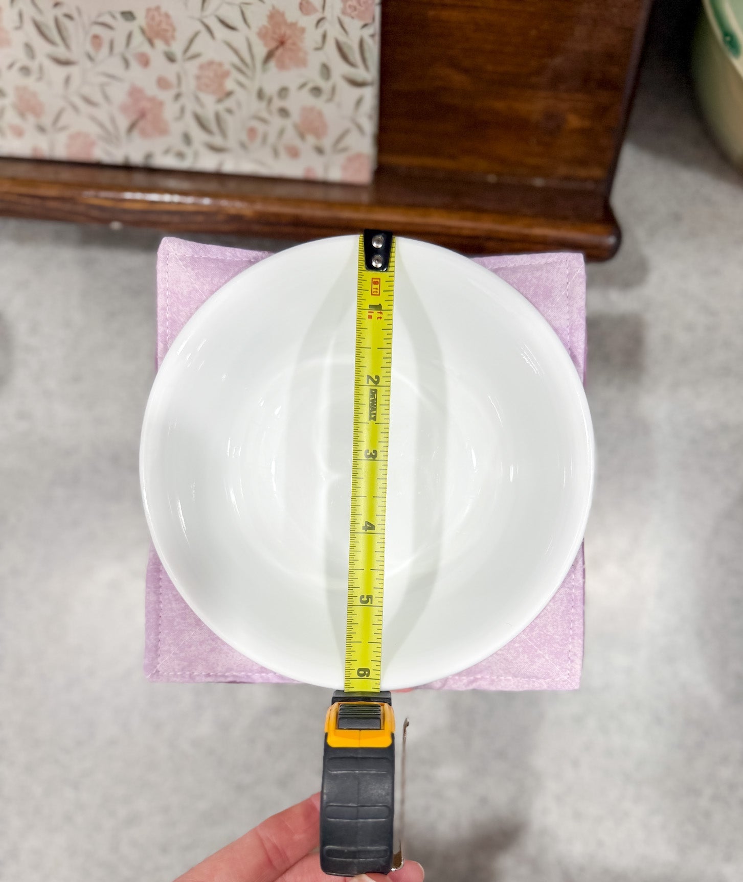 Person measuring a white plate with a tape measure on a gray surface.