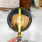 Person measuring a ceramic bowl with a liquid using a tape measure.