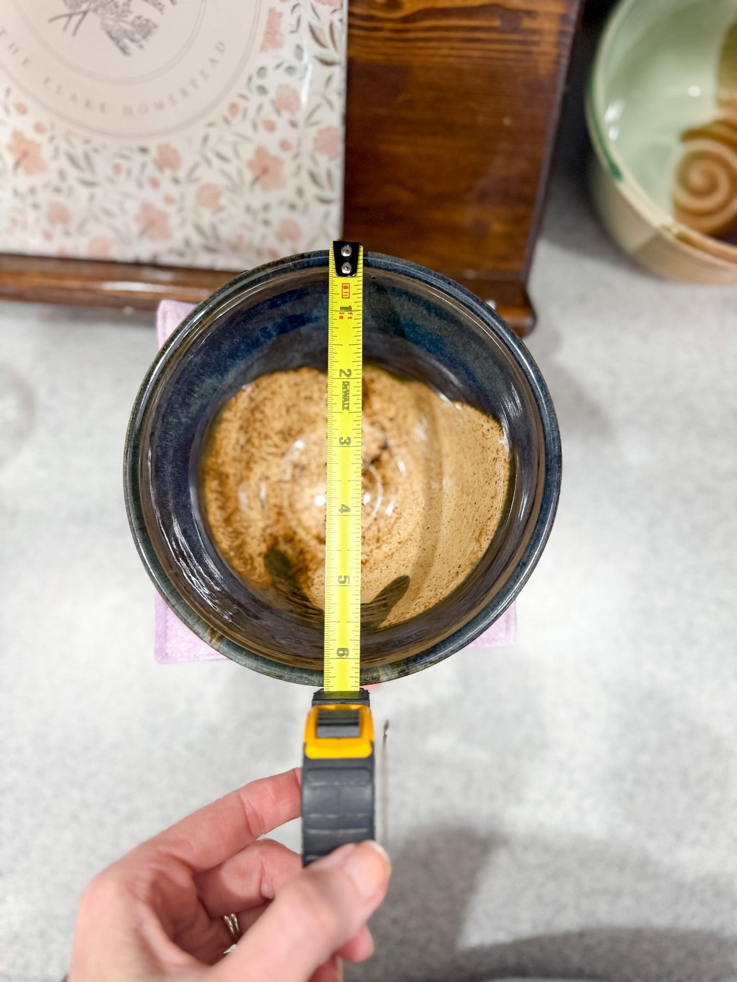 Person measuring a ceramic bowl with a liquid using a tape measure.
