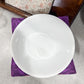 White bowl on a purple napkin with a floral patterned box in the background