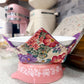 Floral-patterned container on a pink base with kitchen appliances in the background