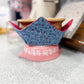 Decorative blue and red fabric-covered object on a pink stand with kitchen background