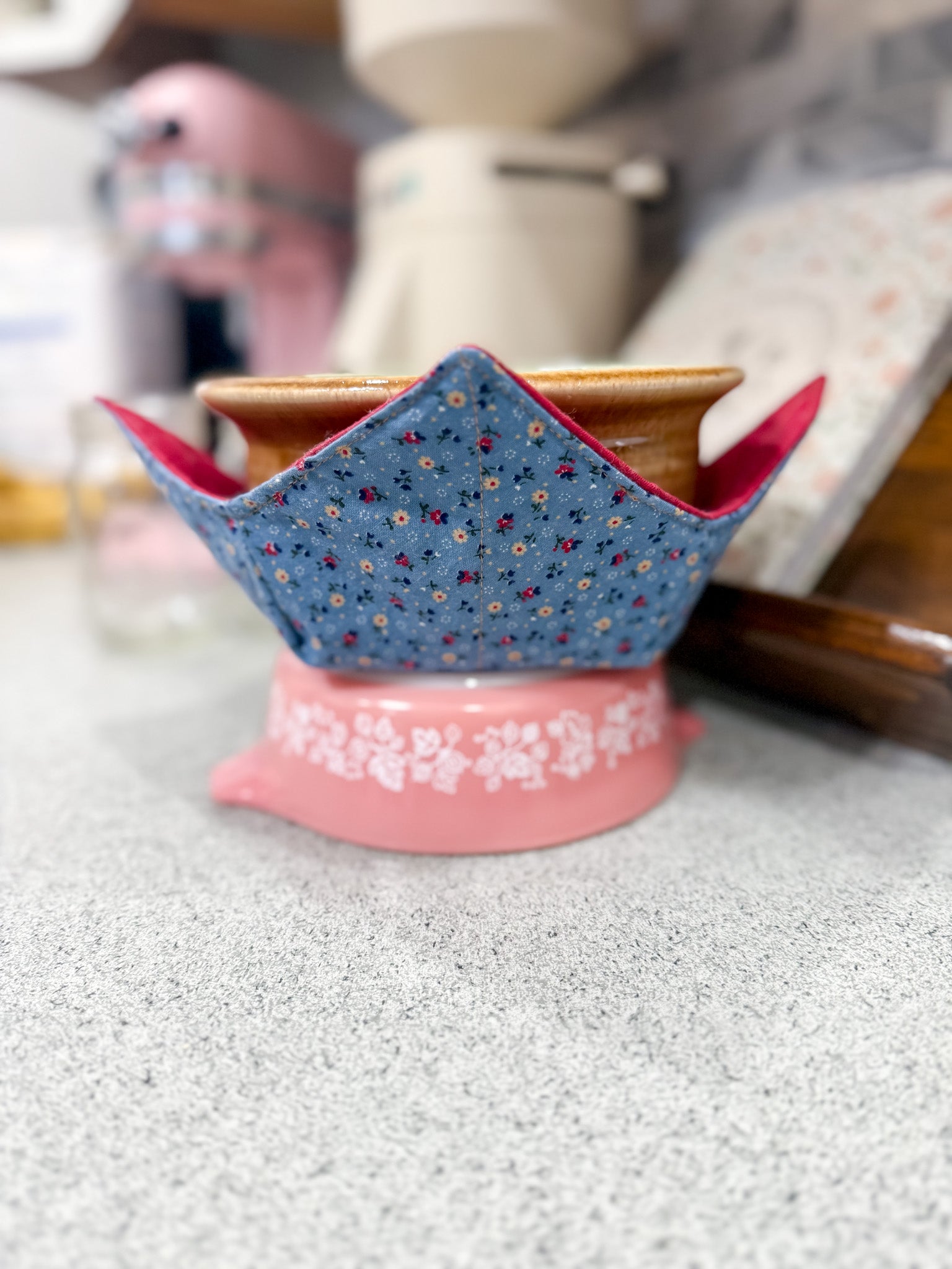 Decorative blue and red fabric-covered object on a pink stand with kitchen background