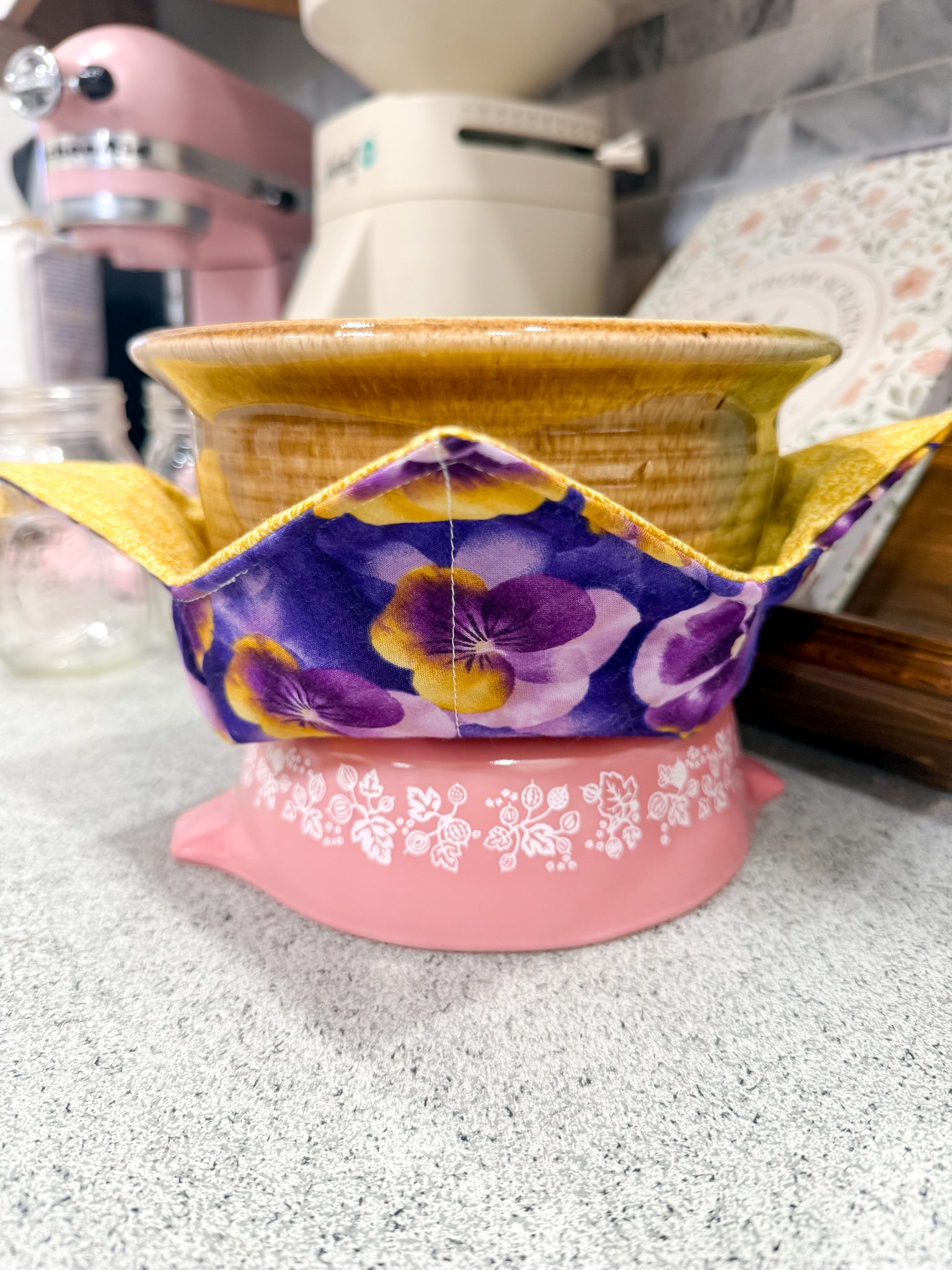 Decorative pot with floral design on a pink base, placed on a countertop.