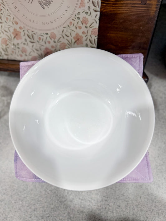 White ceramic bowl on a purple napkin with a floral-patterned dishcloth in the background.