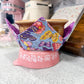 Colorful butterfly-patterned tea cozy on a pink stand in a kitchen setting