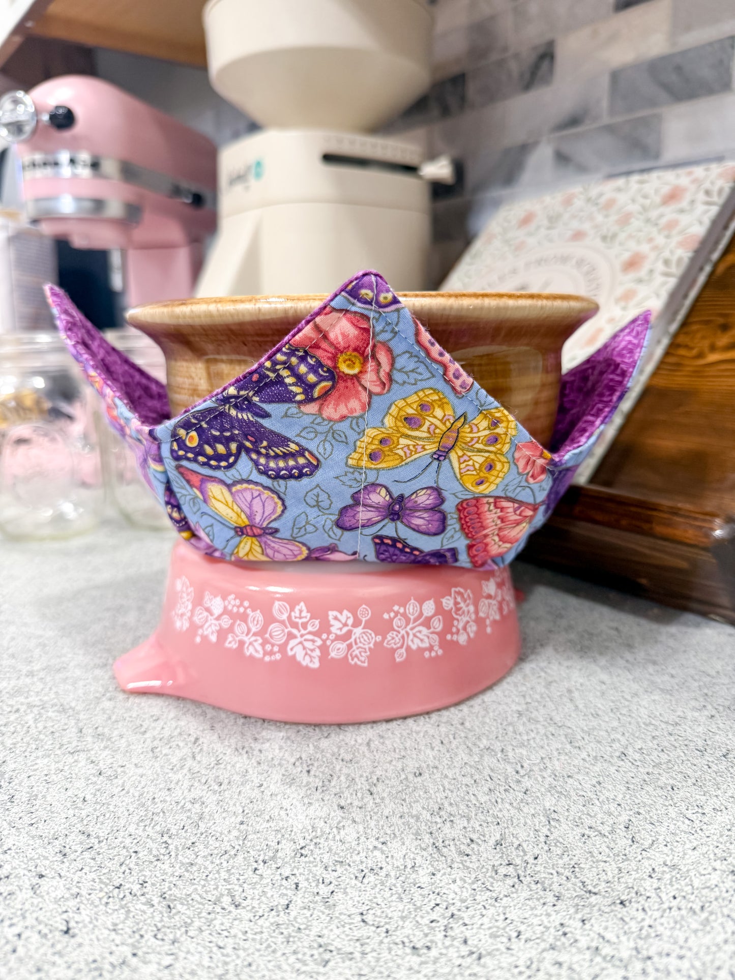 Colorful butterfly-patterned tea cozy on a pink stand in a kitchen setting