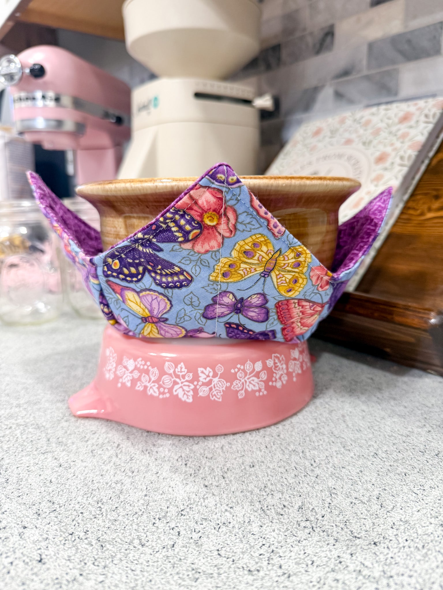 Colorful butterfly-patterned tea cozy on a pink stand in a kitchen setting
