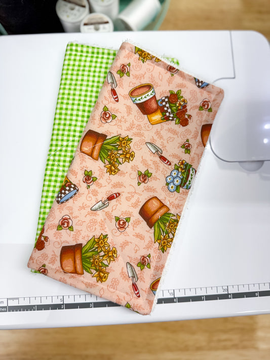 Two fabric swatches on a cutting mat with a ruler, one green checkered and one with rustic patterns.