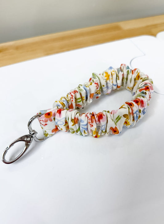 Colorful keychain with floral pattern on a white surface with ruler for scale.