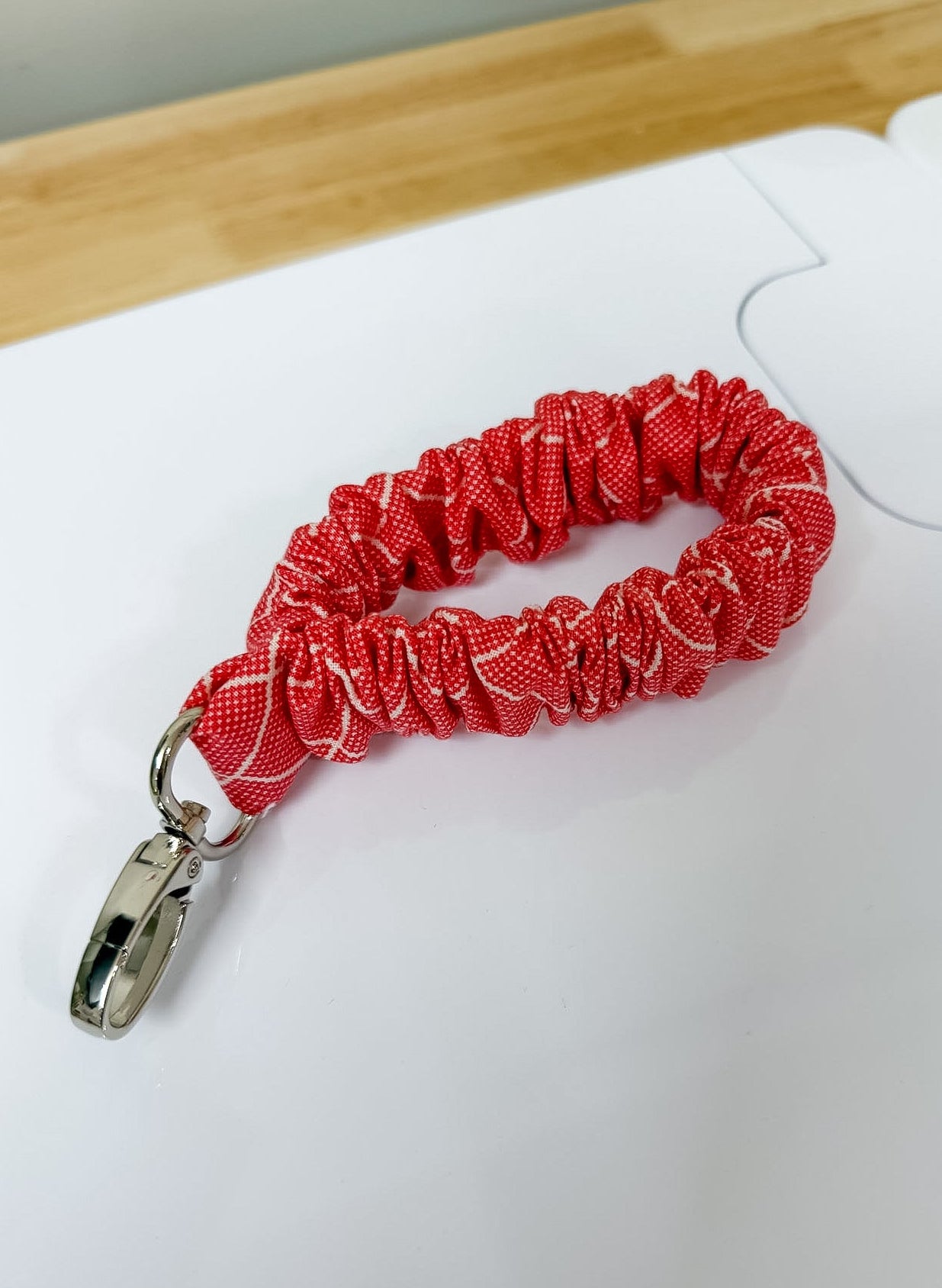 Red scrunchie keychain on a white surface with a ruler for scale.