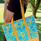 Woman holding a colorful tote bag with floral and checkered patterns in an outdoor setting.