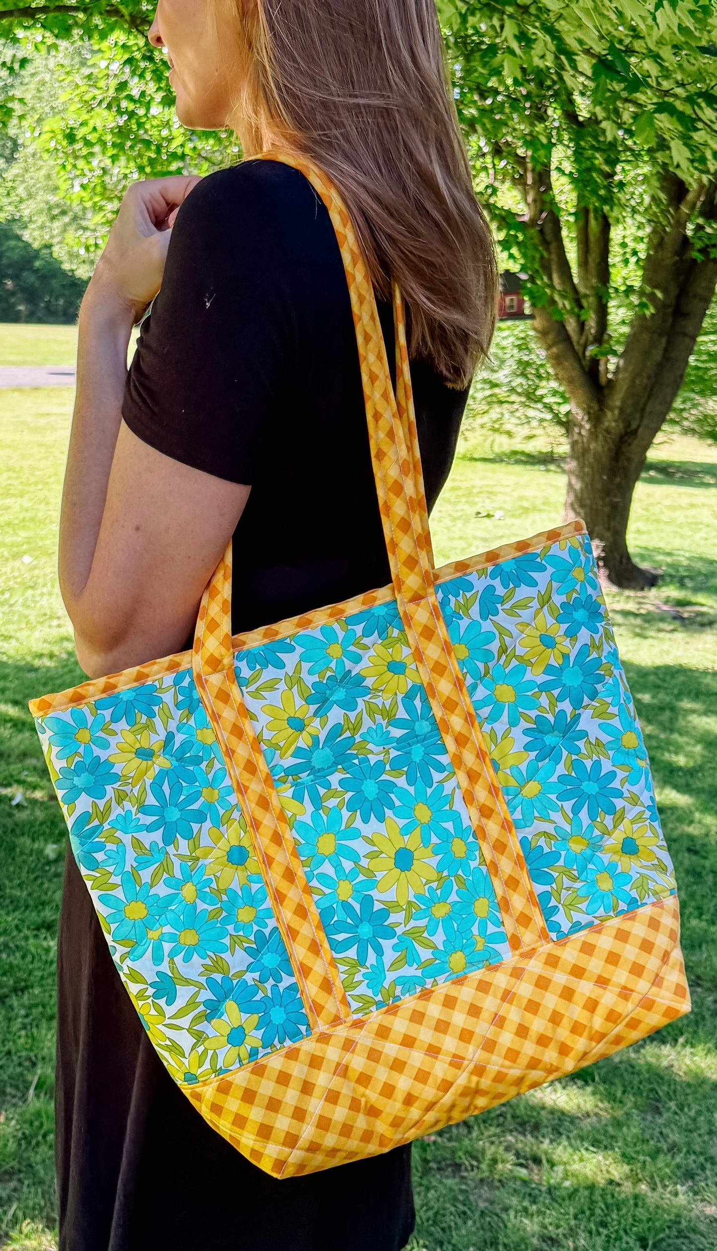 Woman holding a colorful tote bag with floral and checkered patterns in an outdoor setting.