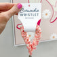 Pink scrunchie wristlet held by a hand with a blurred background