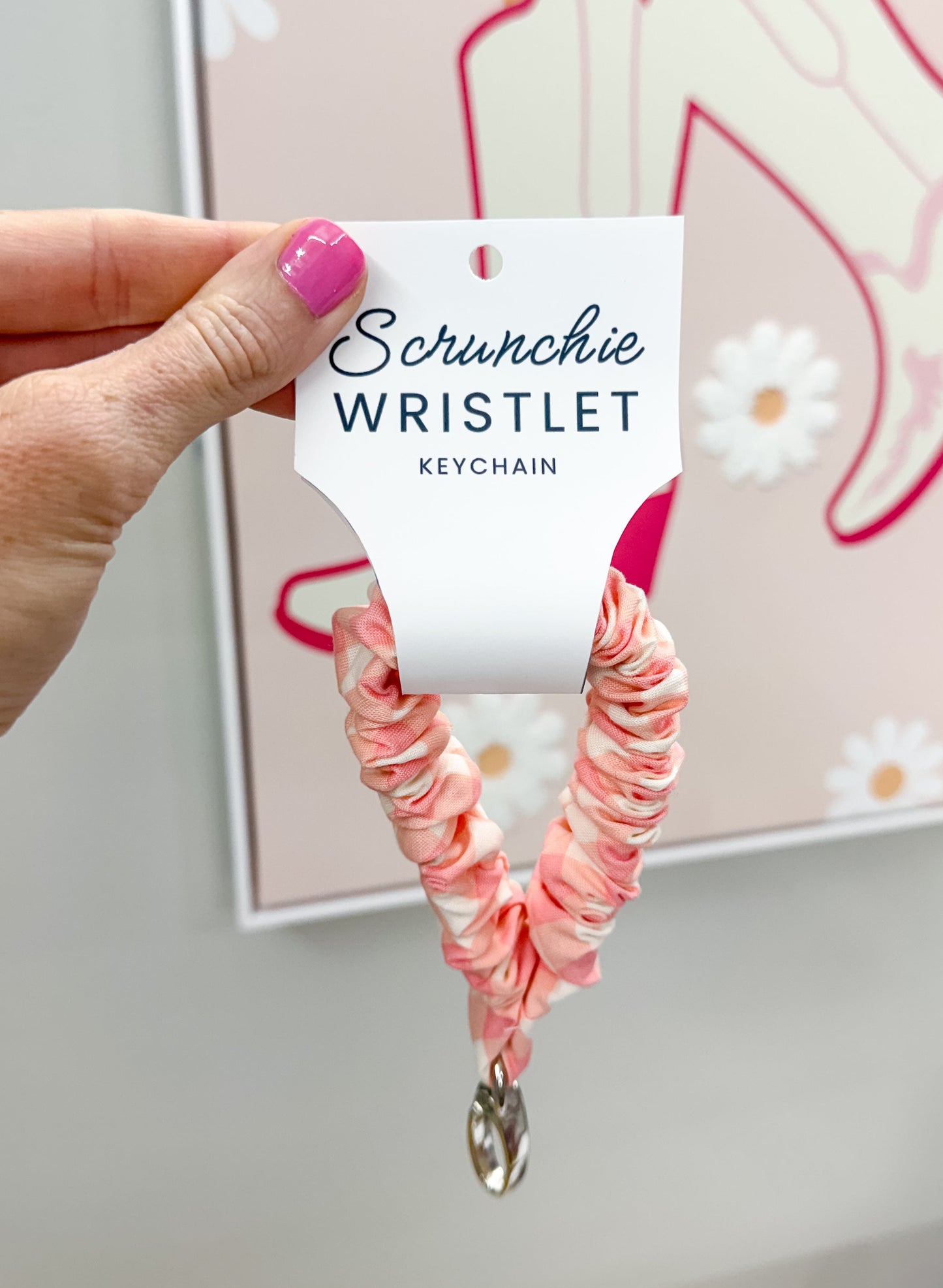 Pink scrunchie wristlet held by a hand with a blurred background